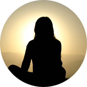 A woman seated cross-legged on a mountain top watching the sunrise